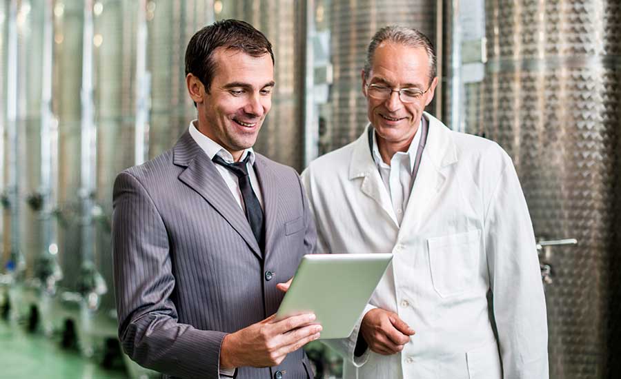 person in suit with tablet talking to white coat food factory manager