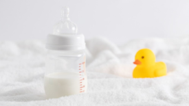 half full baby bottle next to rubber duckie on white surface