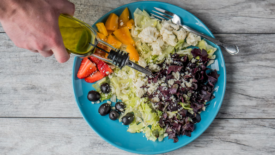 someone pouring olive oil on colorful plate of food