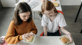 two young girls eating burgers at school lunch